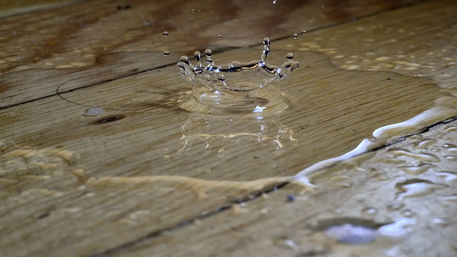 Water droplets and a small splash on weathered wood floor planks